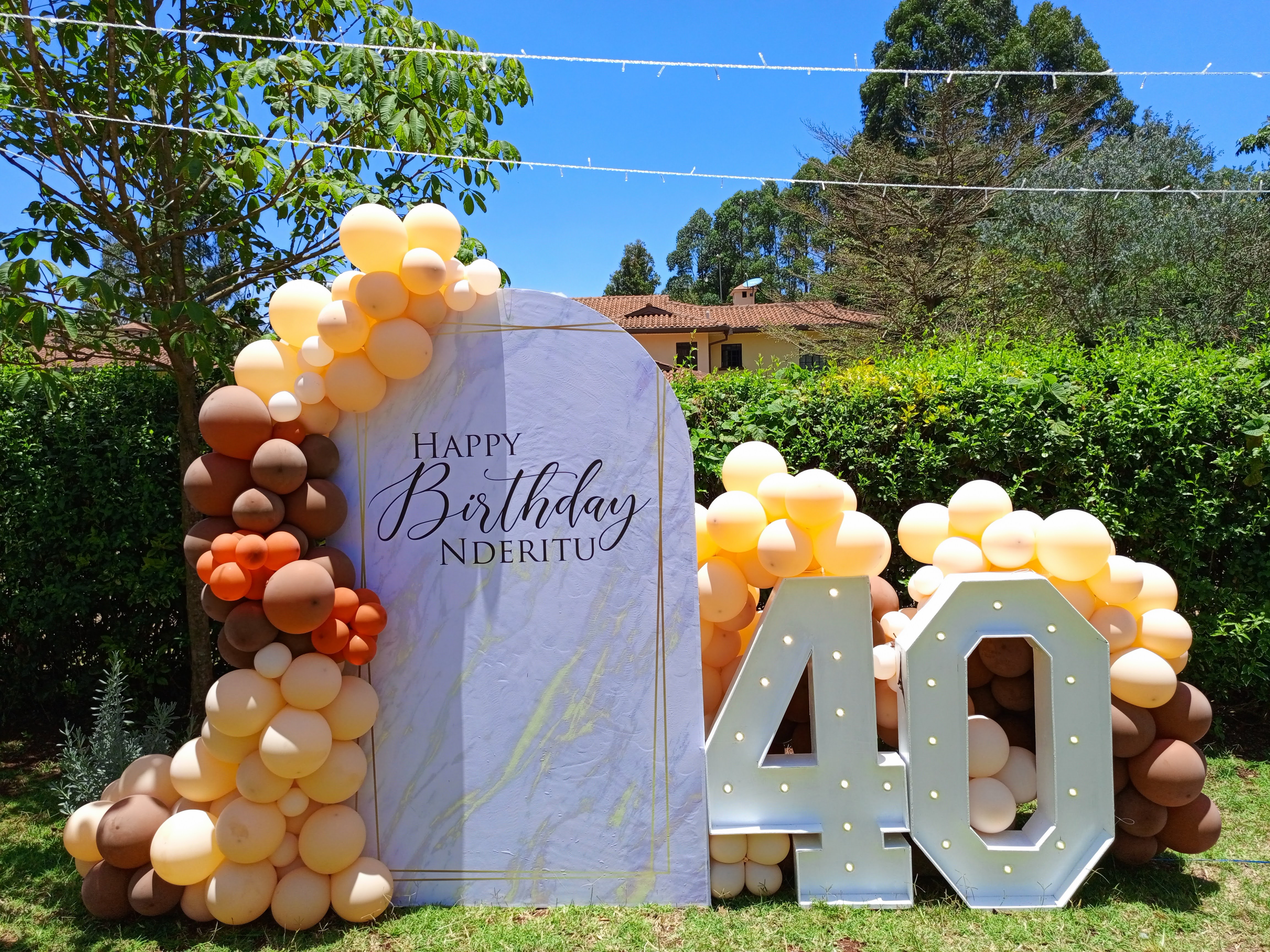 Outdoor 40th birthday backdrop with a marble arch and warm peach and brown balloon garland