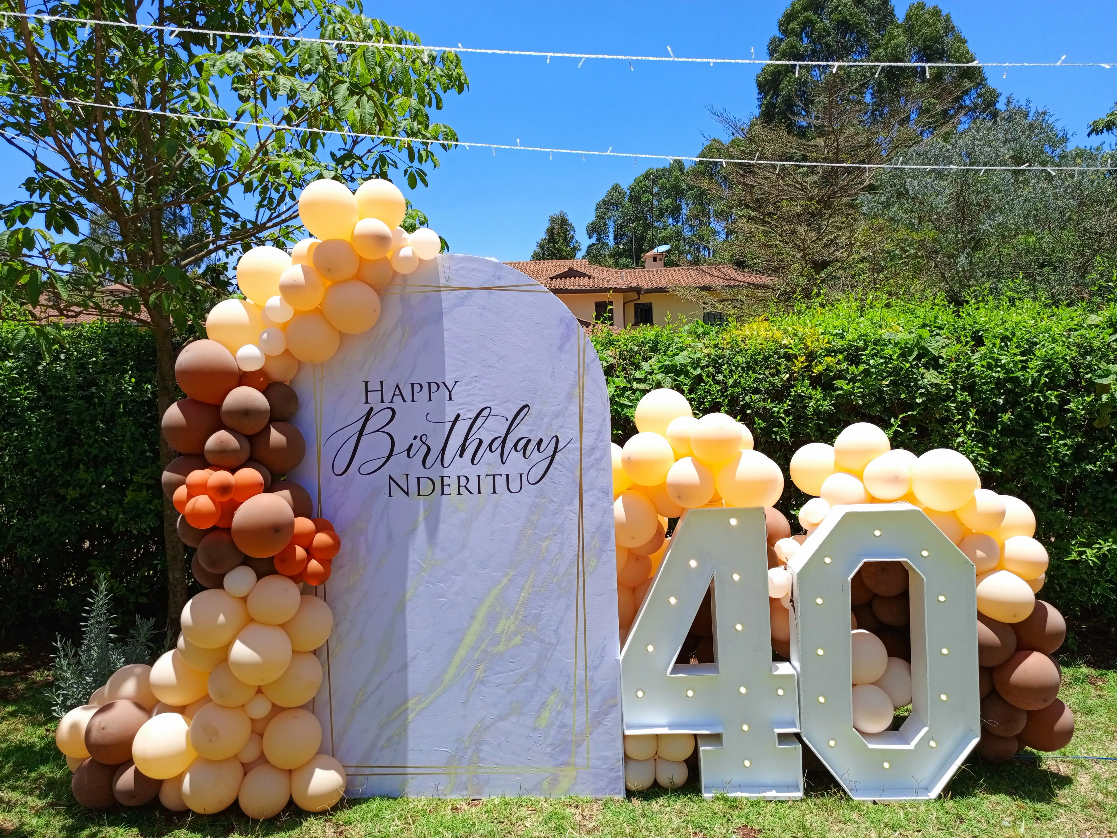 Outdoor 40th birthday backdrop with a marble arch and warm peach and brown balloon garland
