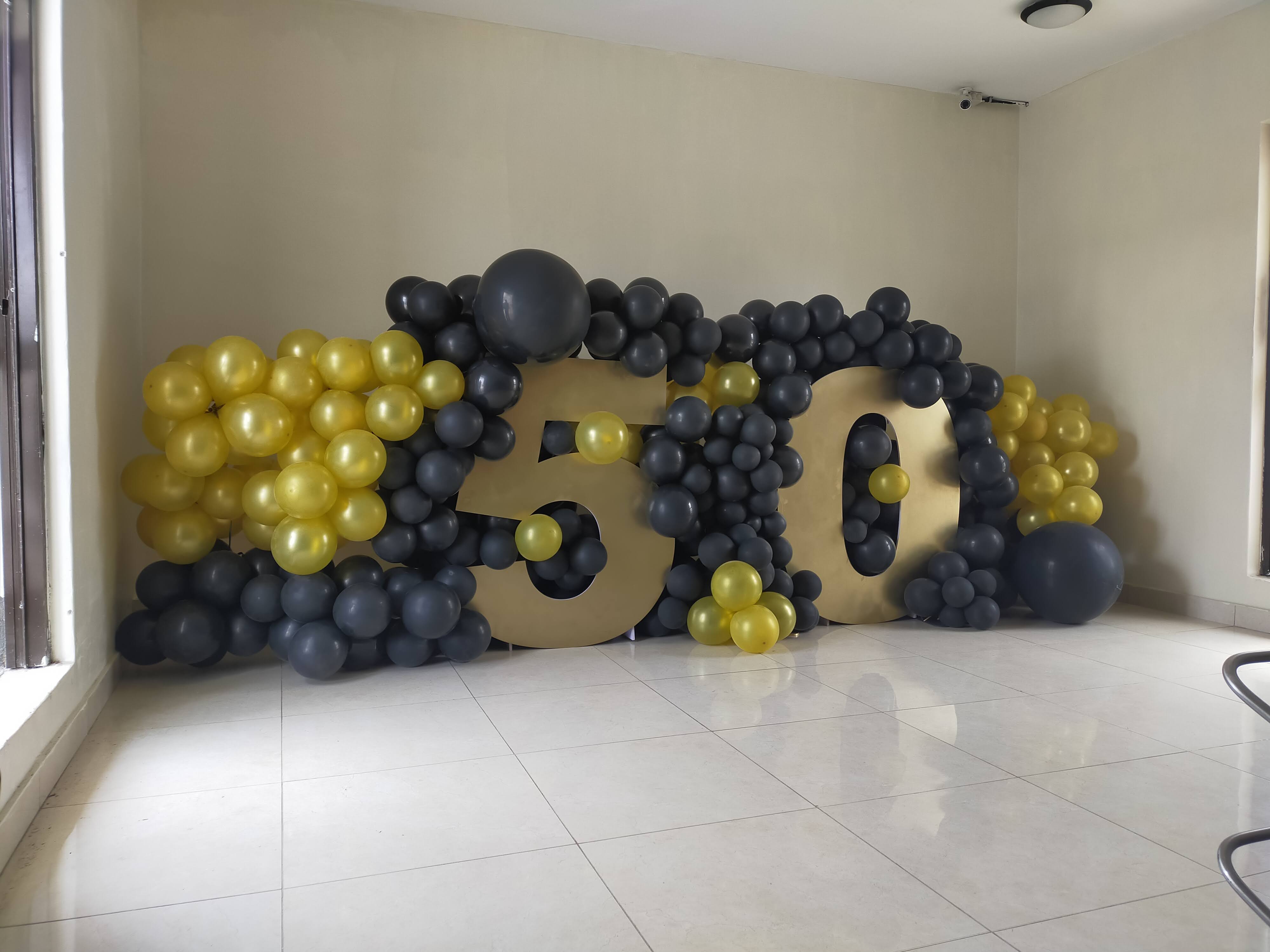 Large gold 50 numerals framed by a black-and-gold organic balloon garland