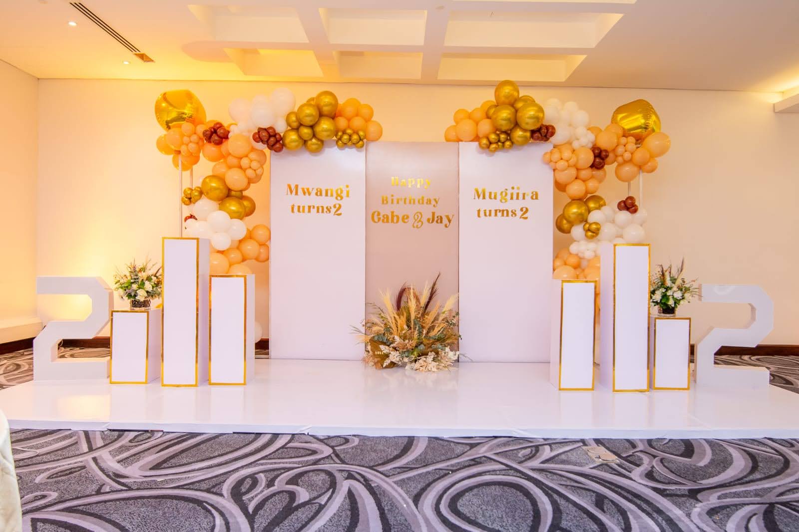 Elegant milestone birthday stage with white plinths and gold balloon clusters