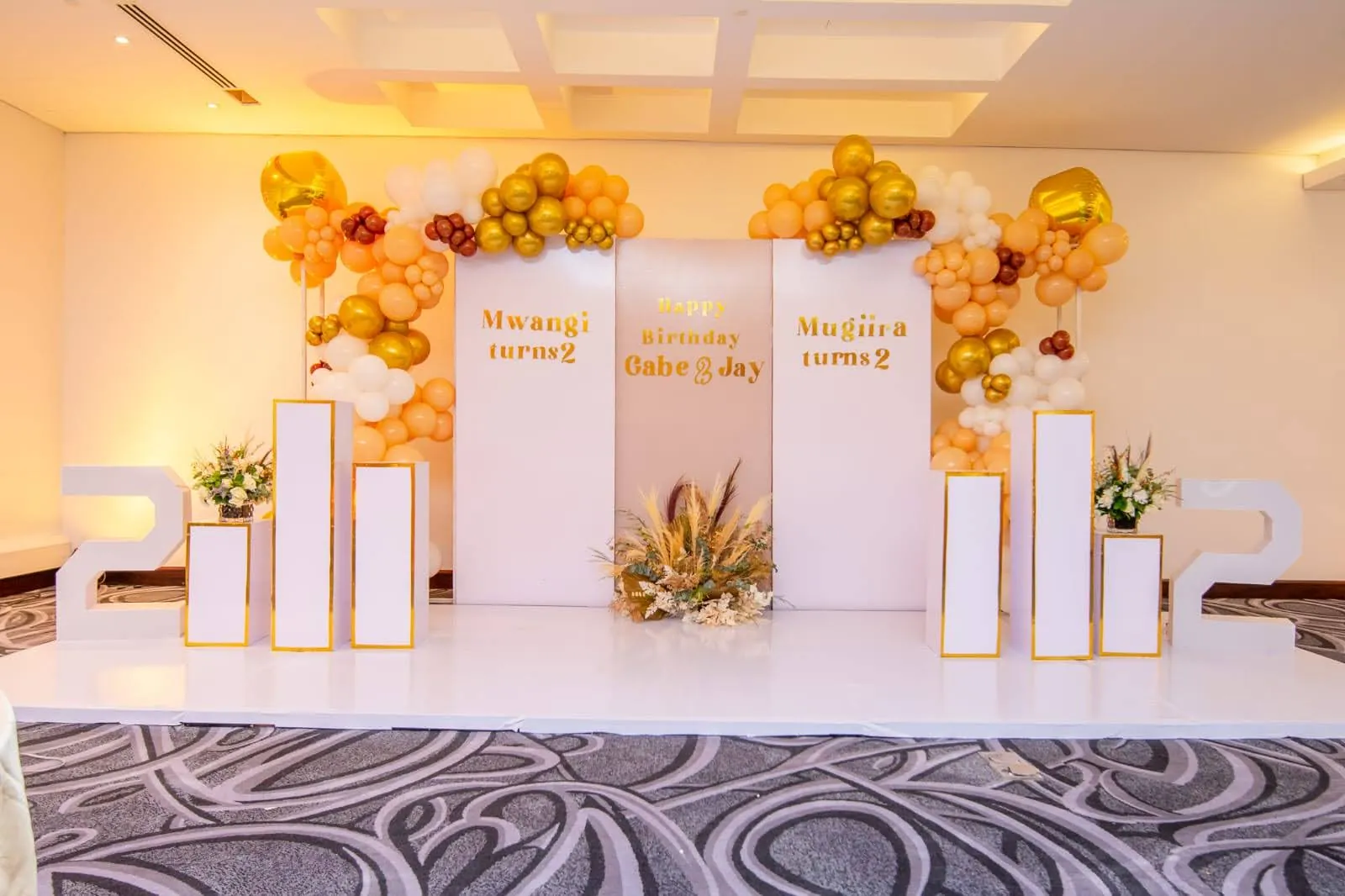 Elegant milestone birthday stage with white plinths and gold balloon clusters