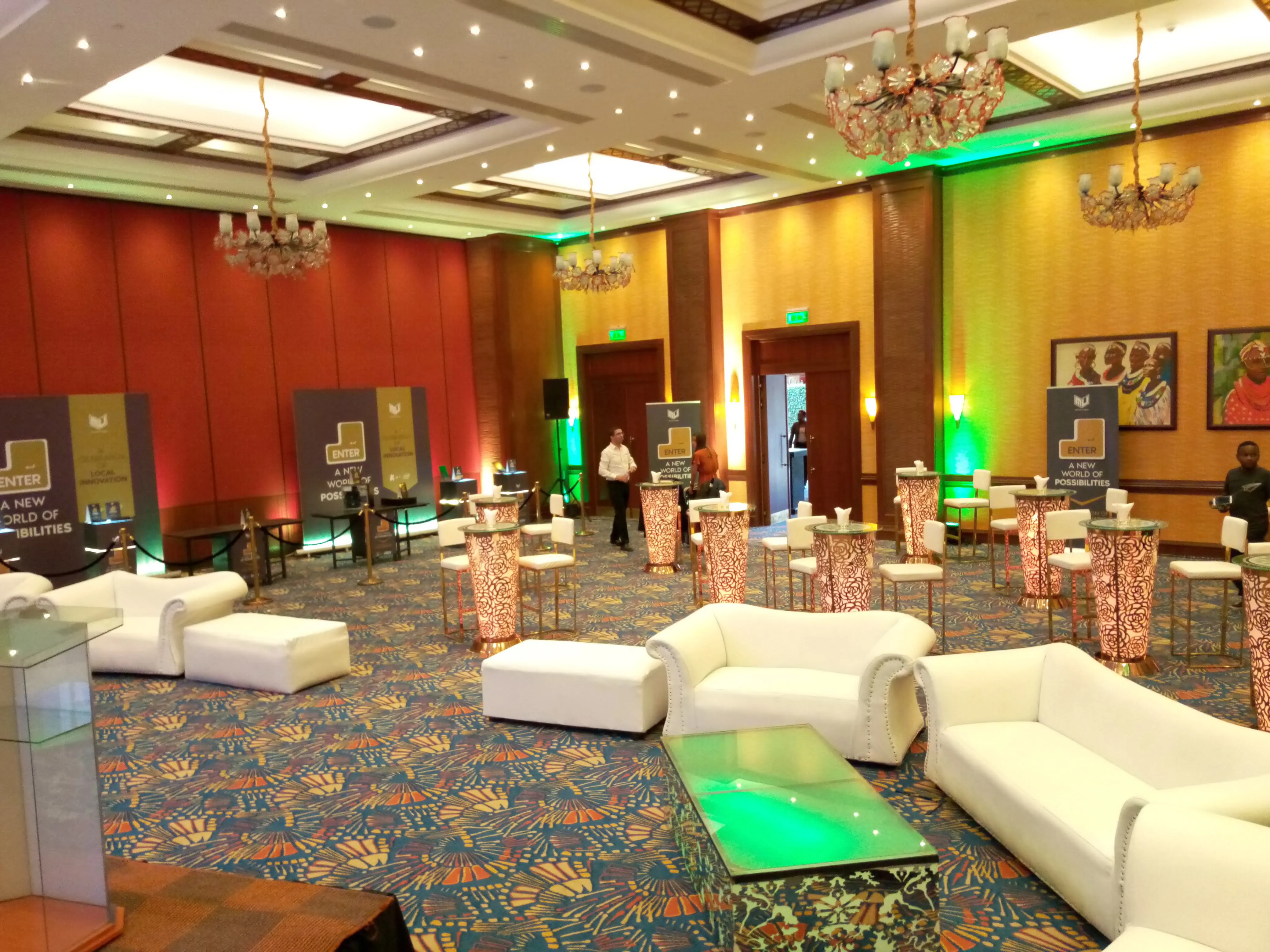 Conference networking lounge with white sofas, lit cocktail tables and red and green uplighting