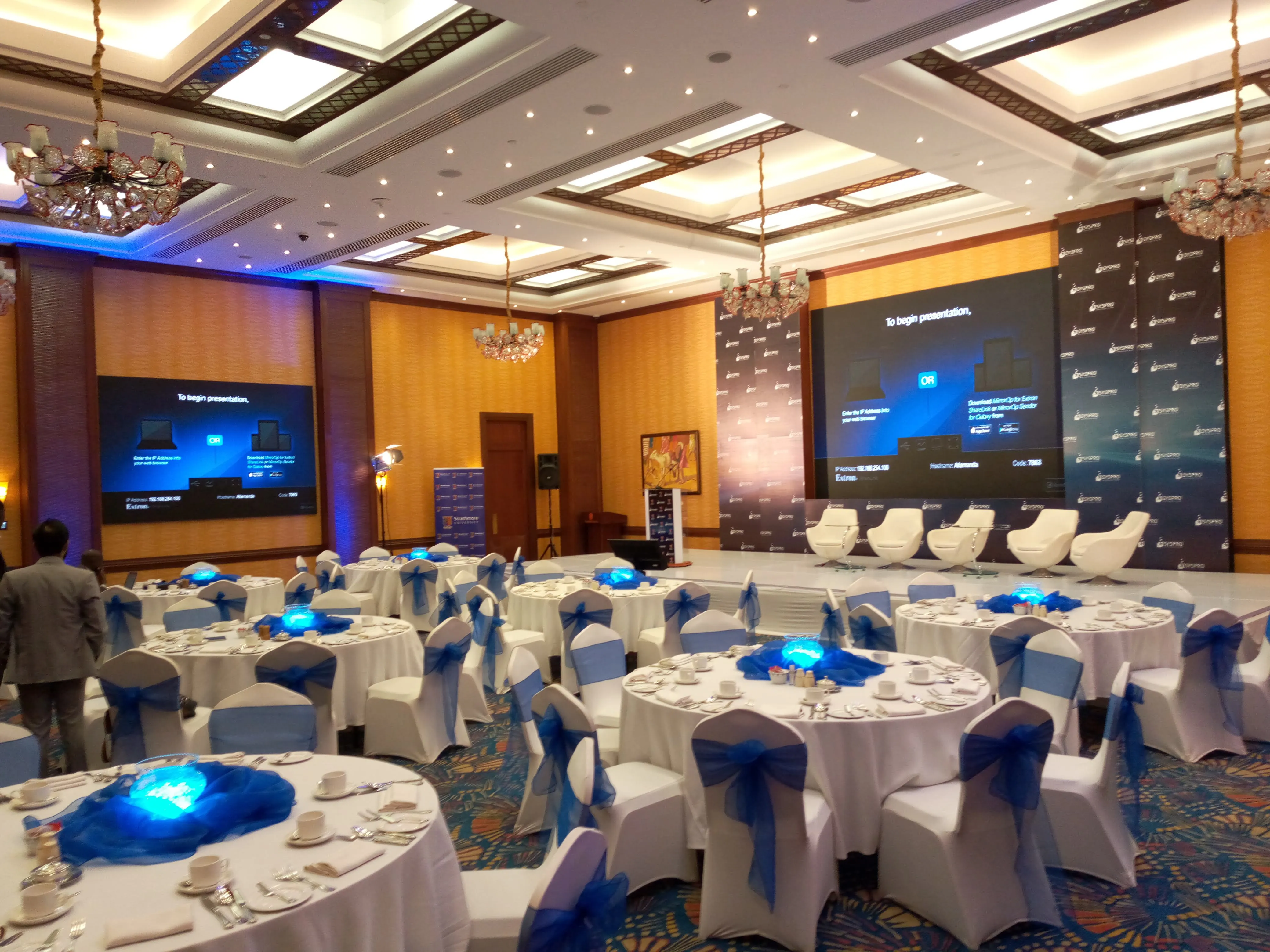 Conference main stage with SYSPRO branded backdrops, white swivel chairs and blue-sashed banquet tables