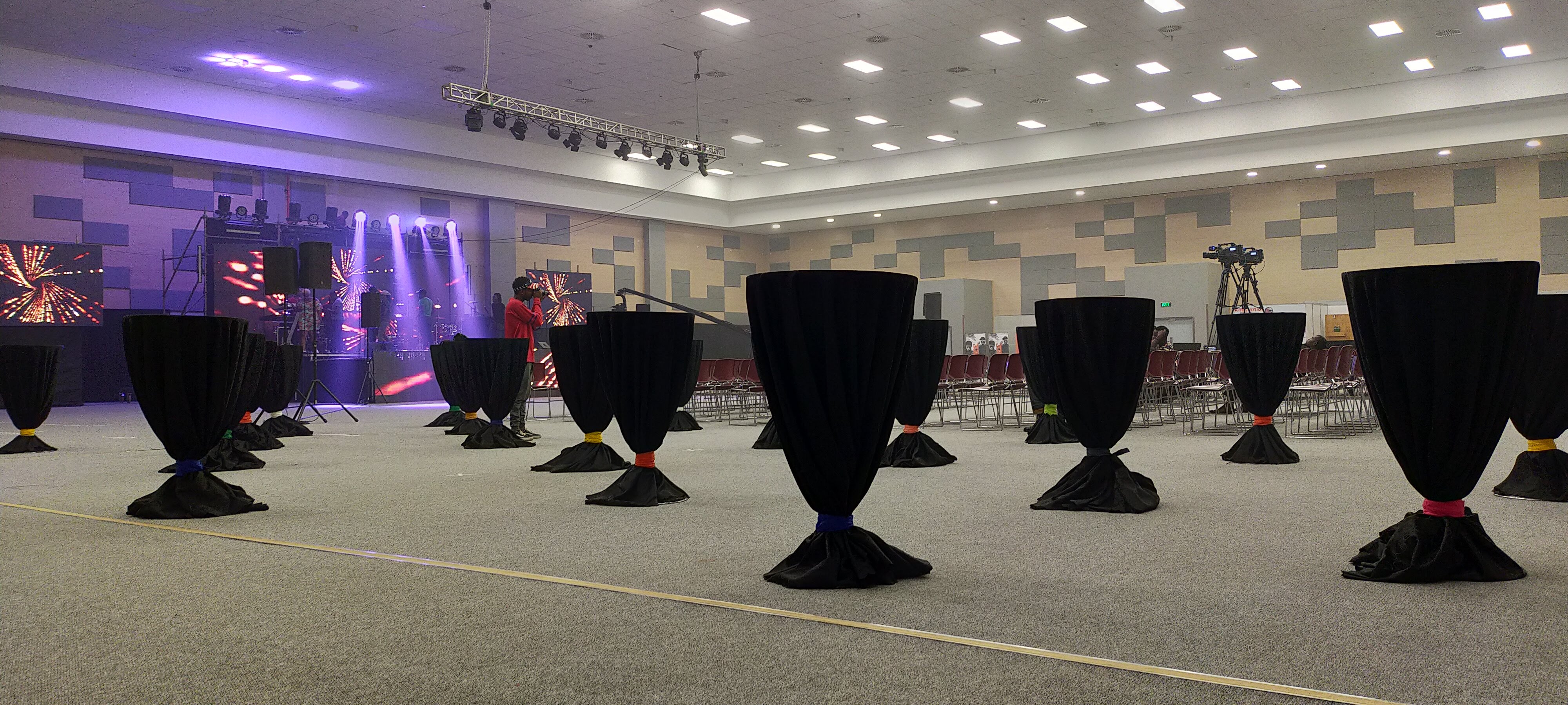 Large hall with black-draped cocktail tables facing a concert stage lit in purple and red
