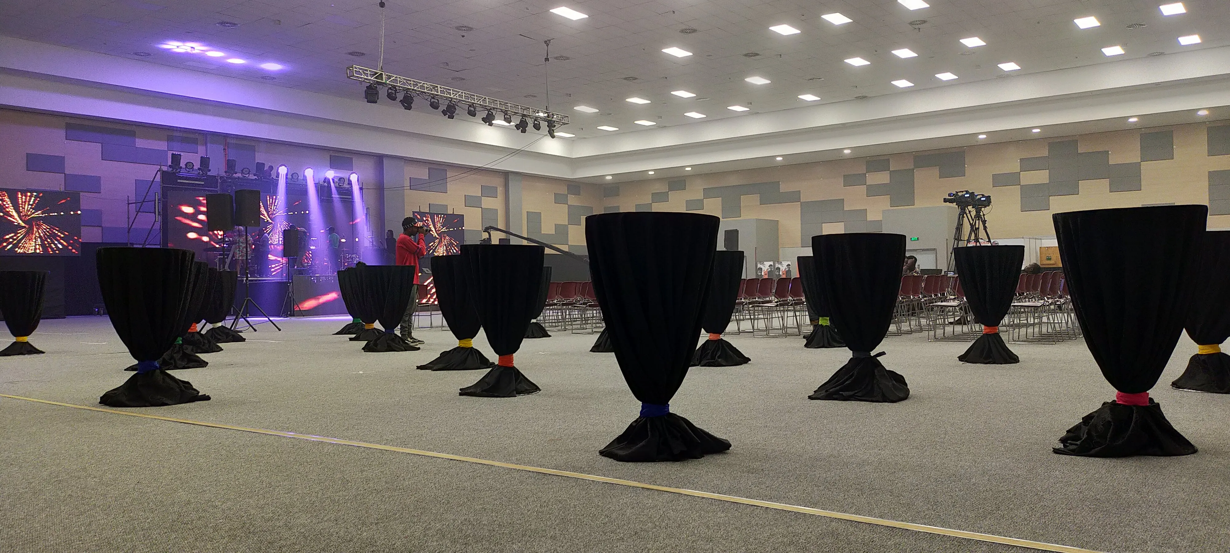 Large hall with black-draped cocktail tables facing a concert stage lit in purple and red