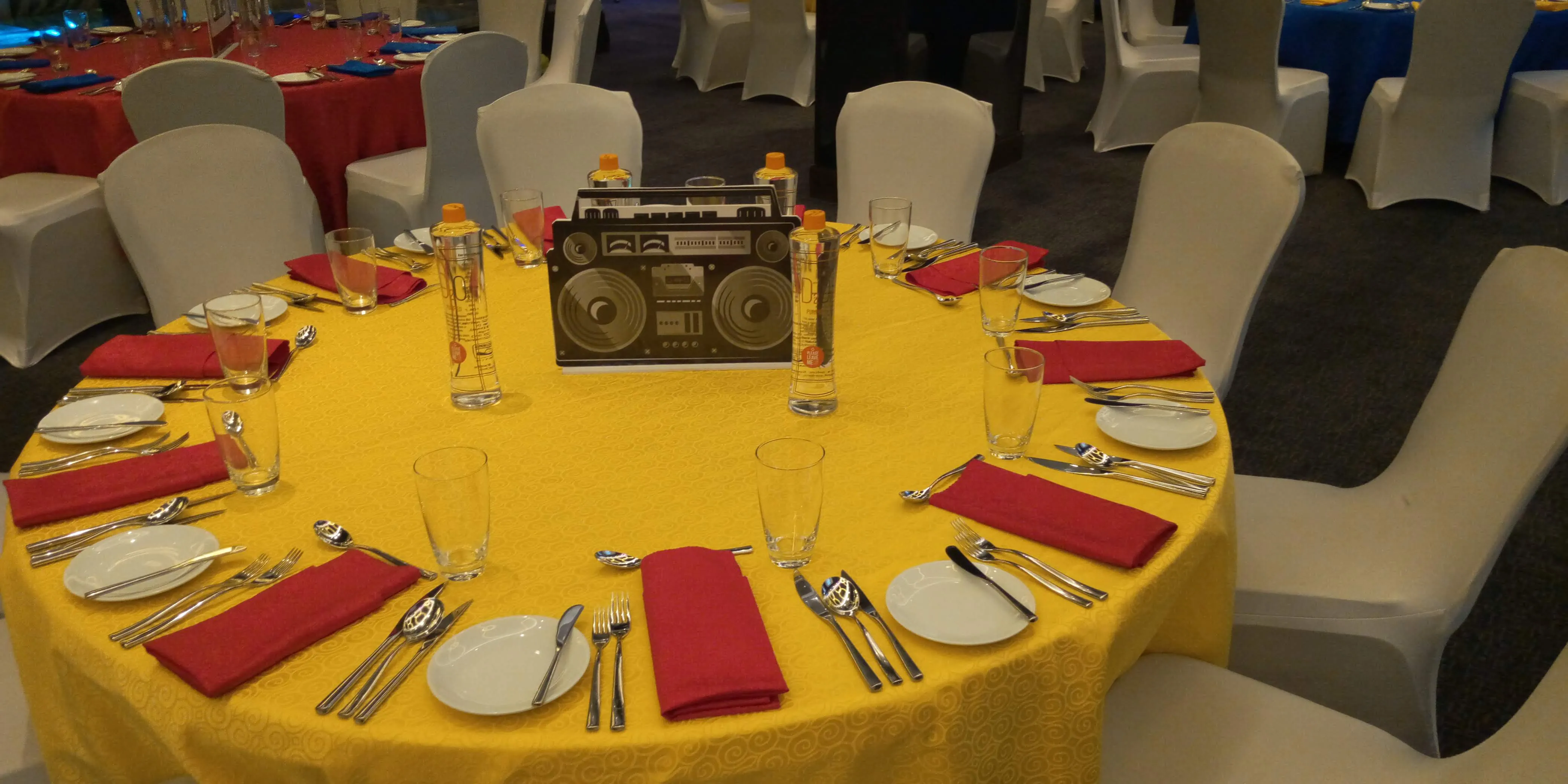 Yellow-linened round table with a cardboard boombox centrepiece and red napkins
