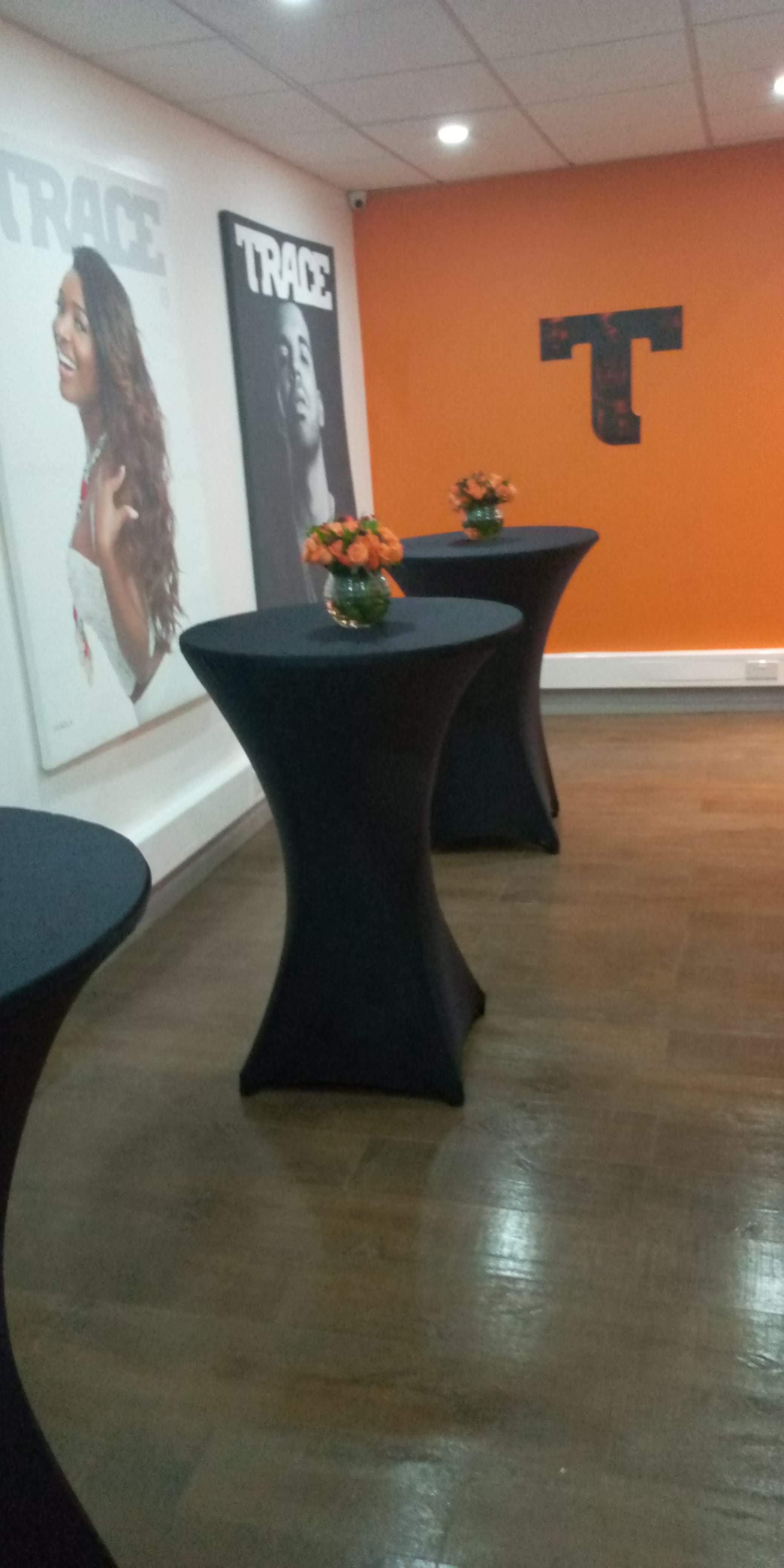 Cocktail tables in black spandex with orange roses against a bold orange TRACE-branded wall