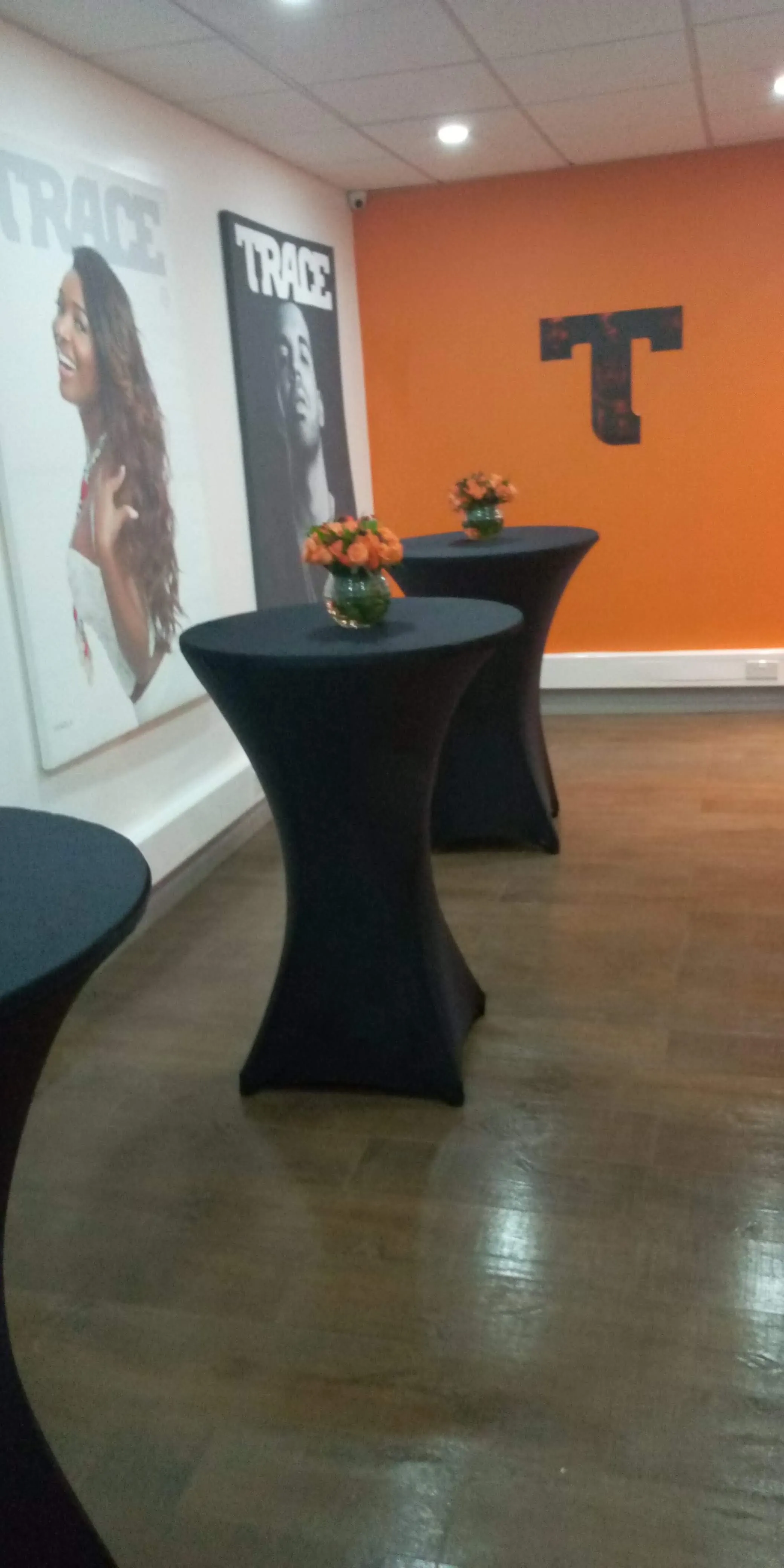 Cocktail tables in black spandex with orange roses against a bold orange TRACE-branded wall