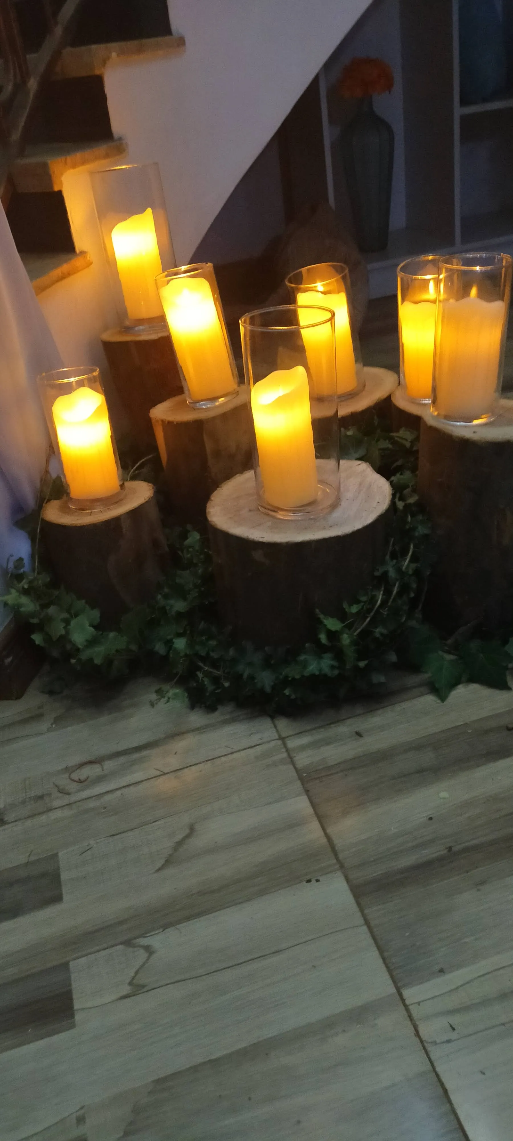 Pillar candles in glass on log rounds, wrapped in ivy, at the foot of a staircase